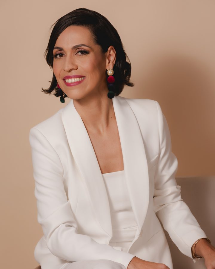 Dra. Cinara Costa sorrindo, sentada, de terno branco